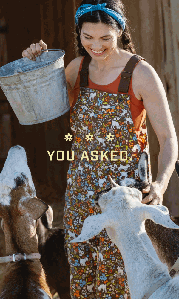 Woman feeding goats while wearing overalls that show a goat and flower pattern.