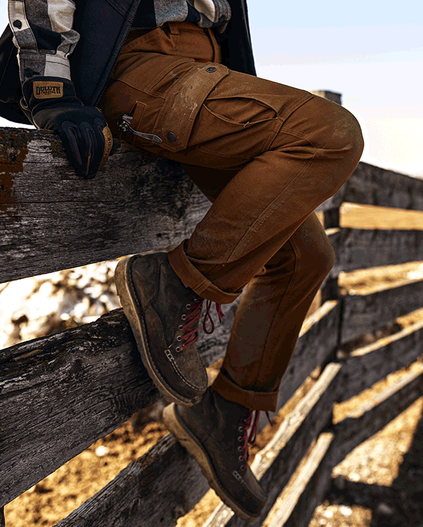 A woman sits on a fence in fire hose pants. Abrasion resistance protects you from pokes