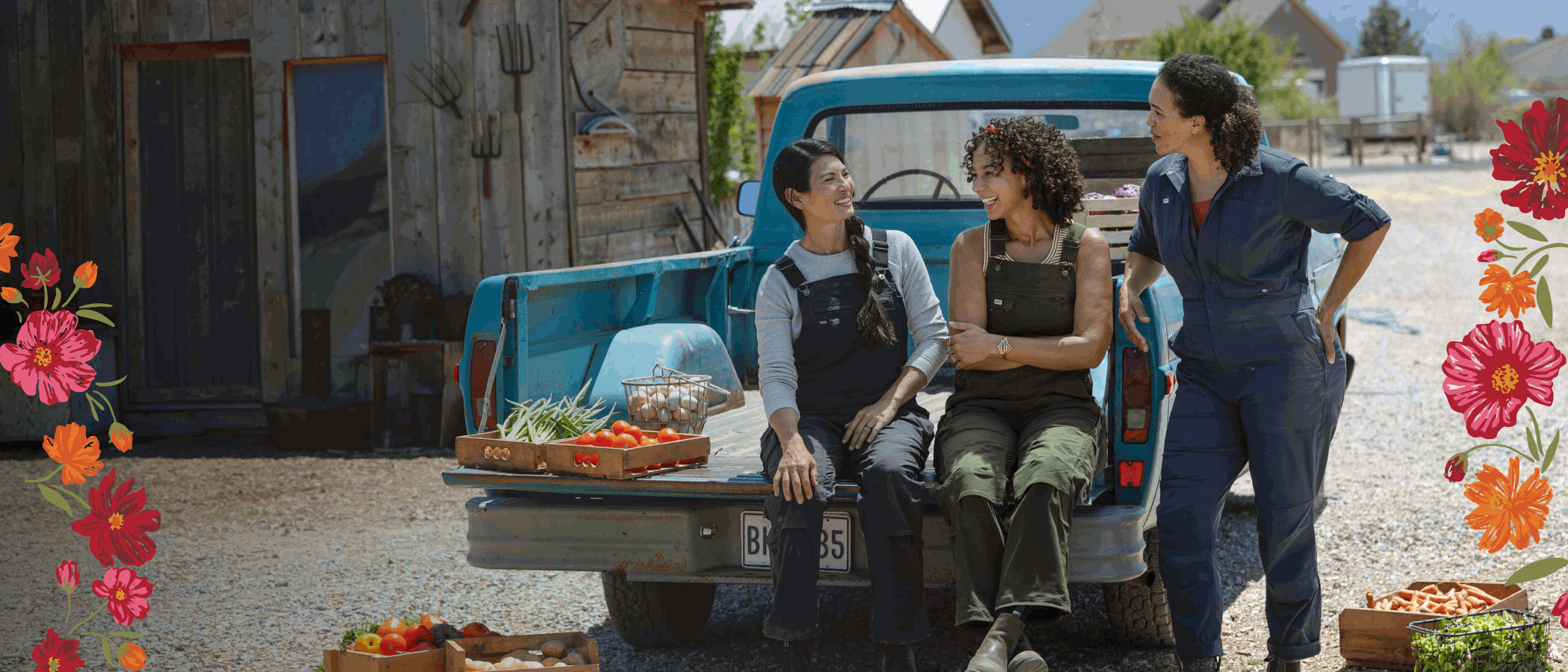 Women wearing overalls, sitting on bed of blue truck.